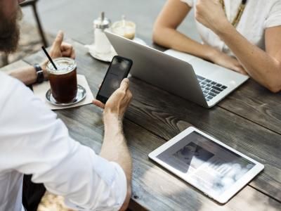Zwei Menschen mit Laptop, Tablet und Smartphone am Tisch